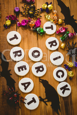 Cookies with trick or treat text by chocolates and decorations on table