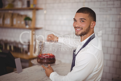 Side view of smiling young waiter holding cake at counter