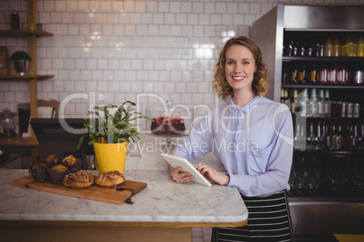 Portrait of attractive young waitress using digital tablet while standing by counter