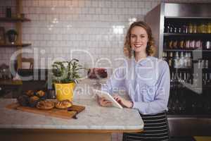Portrait of attractive young waitress using digital tablet while standing by counter