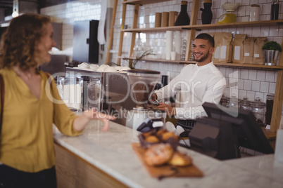 Smiling waiter looking at female customer standing at counter