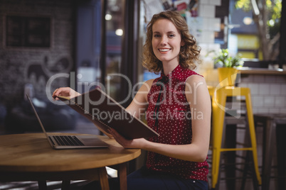 Portrait of smiling young woman holding file while sitting at coffee shop