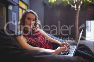Portrait of confident young woman sitting with laptop on bean bag