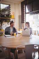 Smiling friends talking while sitting with technologies at coffee shop