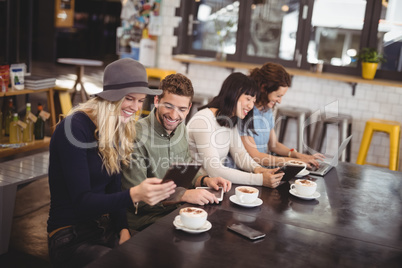 High angle view of happy friends using technologies at table