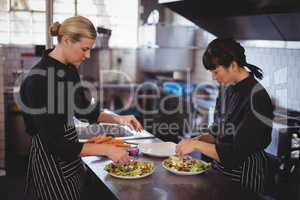 Confident young female chefs preparing Greek salad at kitchen counter