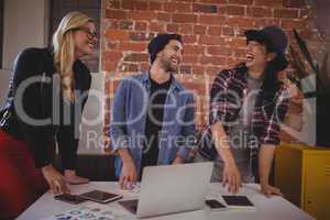 Cheerful young creative team using technologies at coffee shop