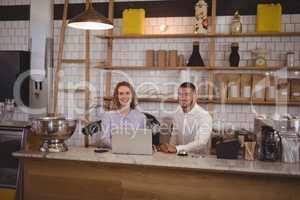 Portrait of smiling waitress and male owner using laptop at counter