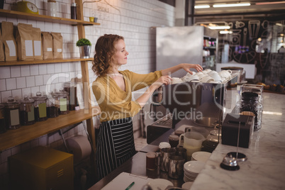 Young waitress arranging cups at counter