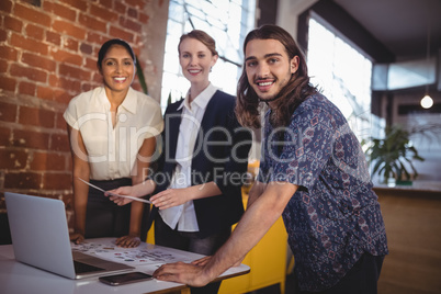 Portrait of smiling young creative team standing with laptop