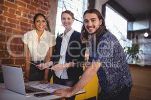 Portrait of smiling young creative team standing with laptop
