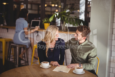 Happy couple talking while sitting with coffee cups and menu at table