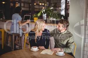 Happy couple talking while sitting with coffee cups and menu at table