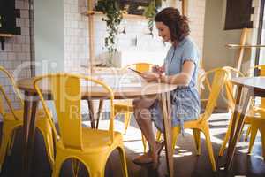 Side view of young woman sitting tablet and papers at coffee shop