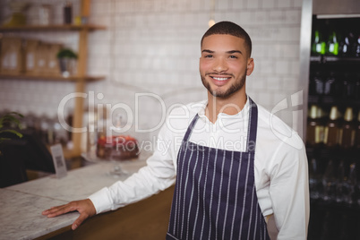 Portrait of smiling handsome waiter standing by counter
