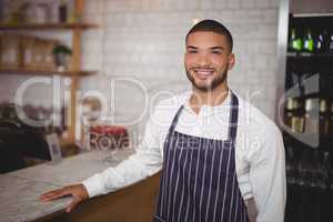 Portrait of smiling handsome waiter standing by counter