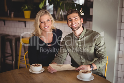 Smiling young couple sitting with coffee cups and menu at table