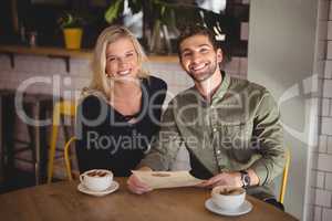 Smiling young couple sitting with coffee cups and menu at table