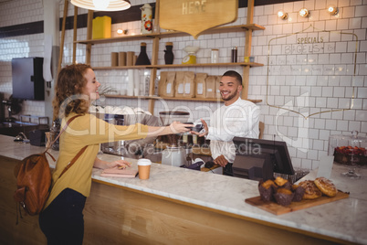 Young woman paying through card to waiter at counter