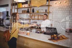 Young woman paying through card to waiter at counter