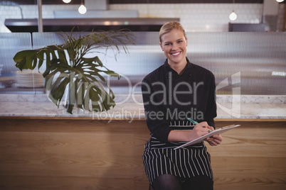 Portrait of young attractive waitress sitting with clipboard