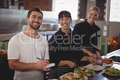 Portrait of waiter with female chefs standing in kitchen Portrait of waiter with female chefs standing in kitchen