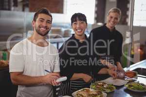 Portrait of waiter with female chefs standing in kitchen