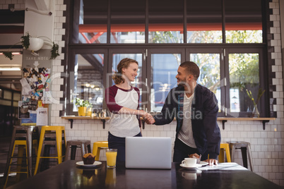 Smiling young man and woman shaking hands at coffee shop