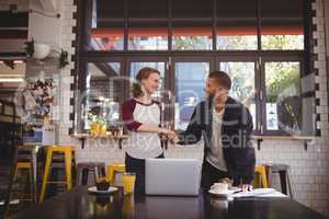 Smiling young man and woman shaking hands at coffee shop