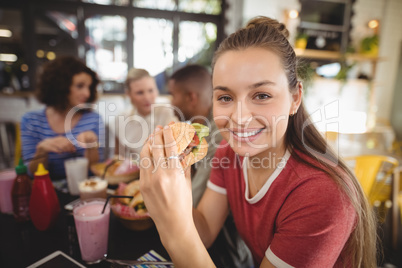 Portrait of smiling beautiful young woman eating burger