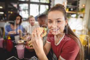 Portrait of smiling beautiful young woman eating burger