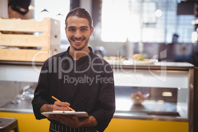 Portrait of smiling young waiter holding clipboard