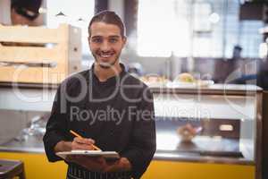 Portrait of smiling young waiter holding clipboard