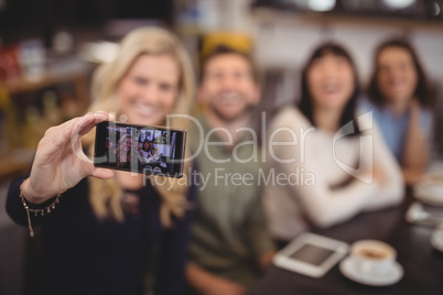 Woman taking selfie with friends from mobile phone at coffee shop