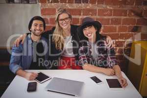 Portrait of smiling creative team sitting with technologies against brick wall