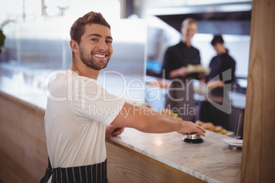 Portrait of smiling waiter pressing bell on counter