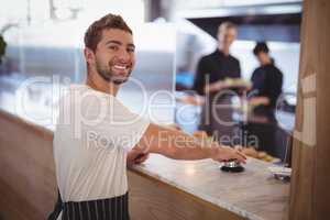 Portrait of smiling waiter pressing bell on counter