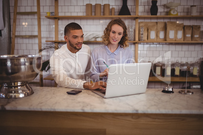 Male owner and young waitress using laptop while sitting at counter