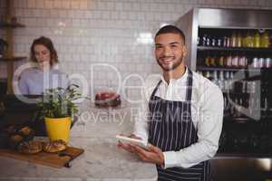 Portrait of smiling young waiter using digital tablet while standing by counter