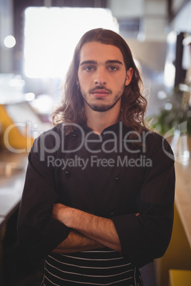 Portrait of confident young waiter standing with arms crossed