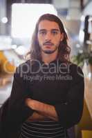 Portrait of confident young waiter standing with arms crossed