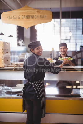 Portrait of smiling young waiter and waitress holding plates at counter