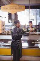 Portrait of smiling young waiter and waitress holding plates at counter
