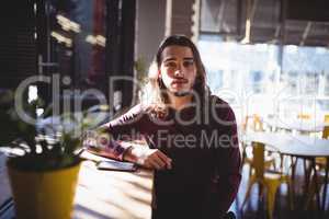 Portrait of young man with long hair sitting at coffee shop