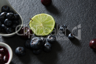 Slice of lemon and spoon with blueberries on black background