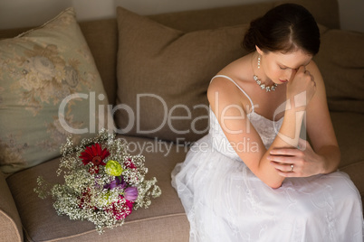 Sad bride sitting by bouquet on sofa at home
