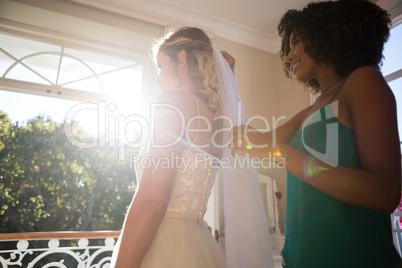 Beautician adjusting veil on bride hair at home