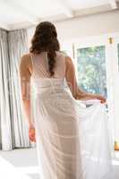 Young bride in wedding dress standing at home