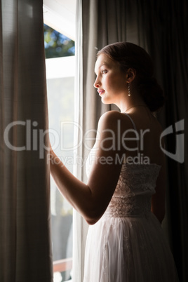 Beautiful bride looking through window while standing in darkroom at home