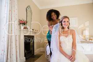 Smiling beautician adjusting veil of bride sitting on bed